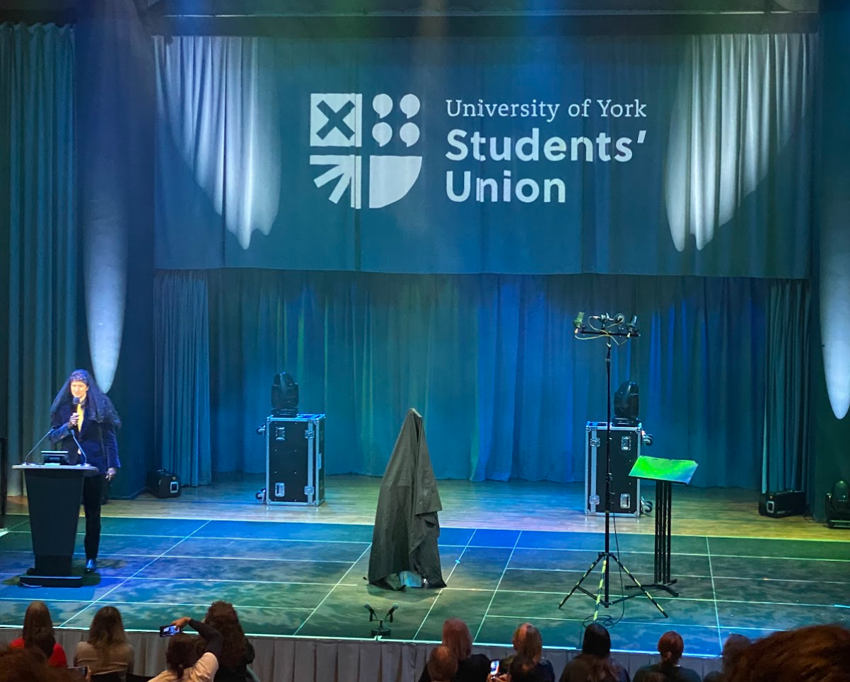 Central Hall stage with the covered Long Boi statue in the middle of the stage. Audience sitting infront.