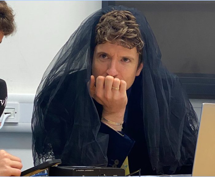 Greg James in discussion with York Vision, looking contemplative and wearing a black veil.