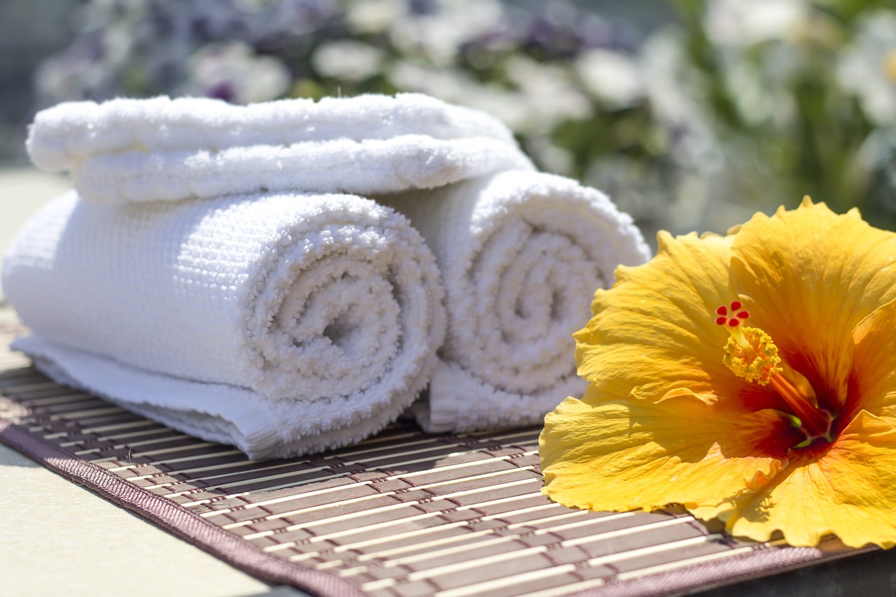 Fluffy white towels with a yellow sunflower on a wooden mat