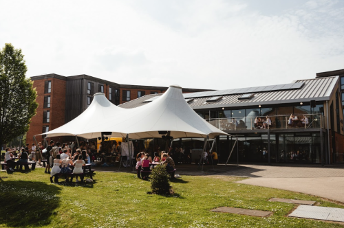 Students enjoying the sun sitting under a white canope on a sunny day on green grass