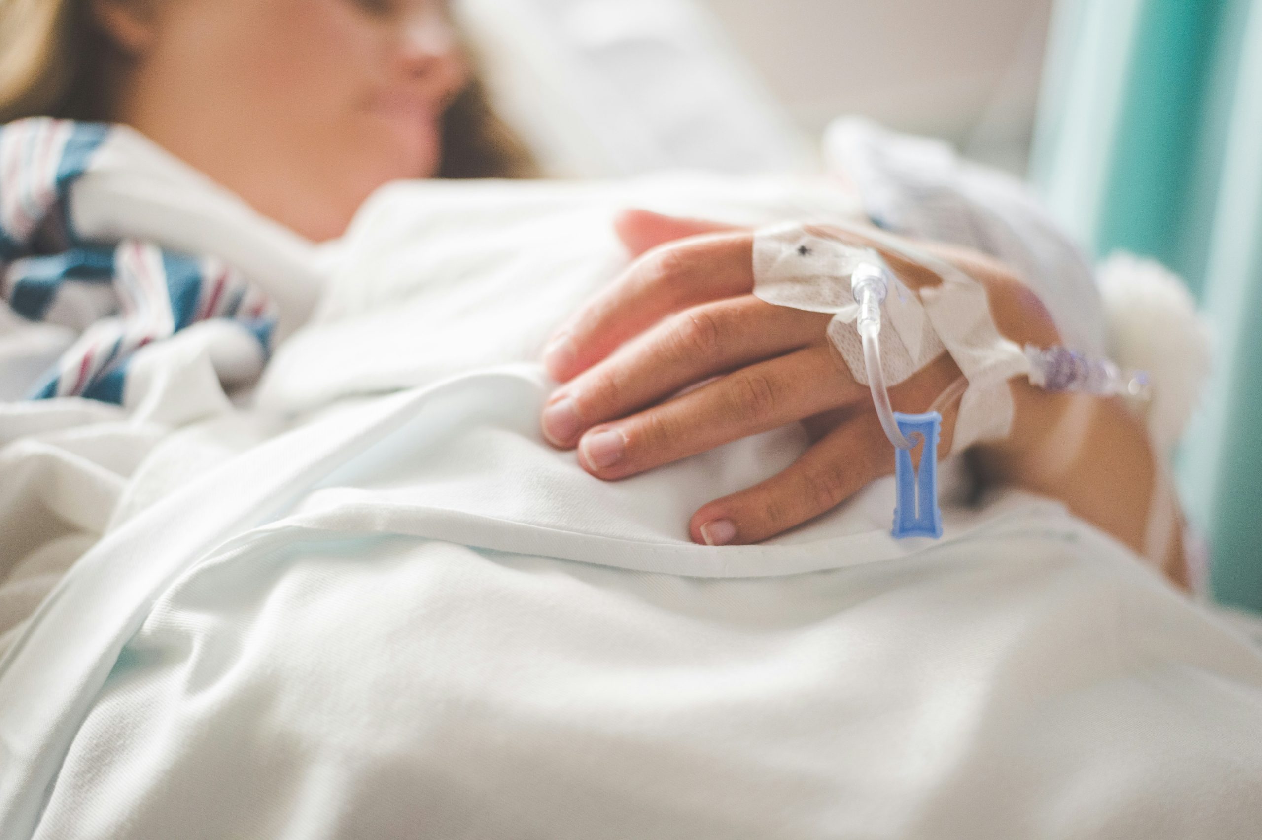 Image of a patient lying in a hospital bed with a drip attached to their hand